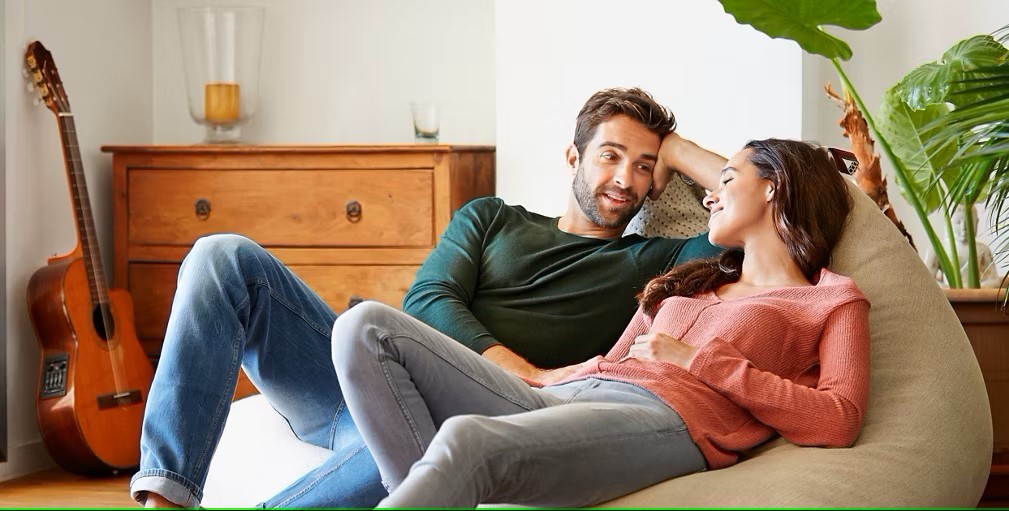 Ein Pärchen sitzt gemütlich auf einem Sitzsack in ihrem Wohnzimmer und unterhalten sich.