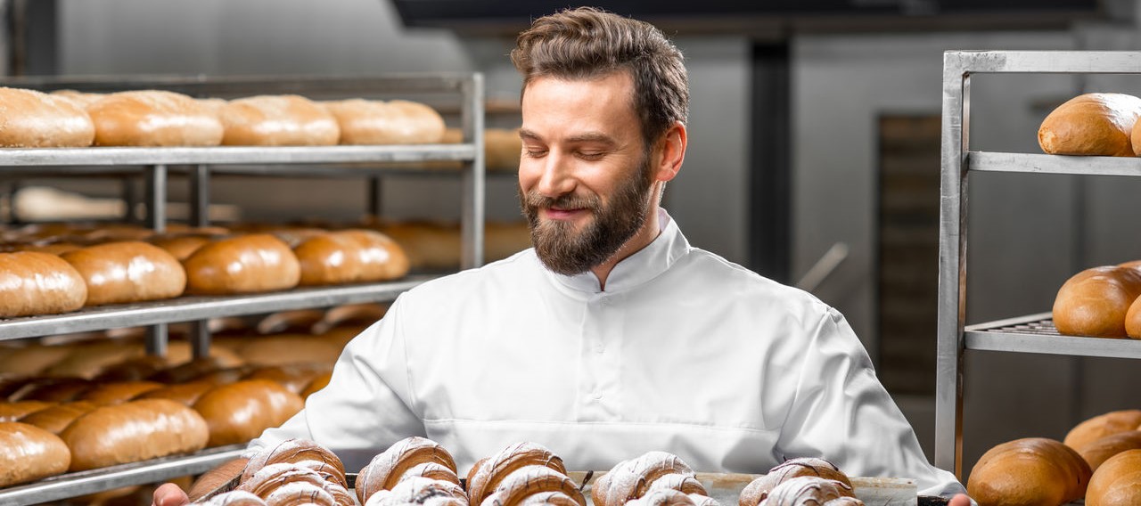 Ein Bäcker lächelt zufrieden seine selbstgebackenen Croissants an.