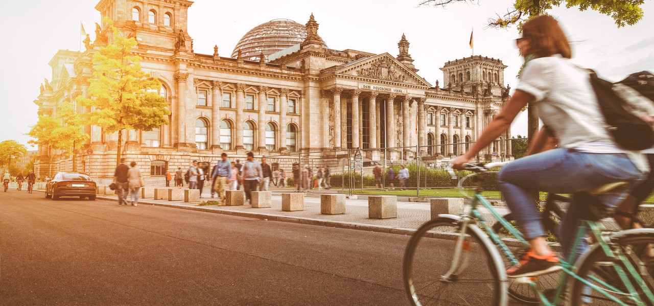 Eine Fahrradfahrerin fährt vorm Berliner Reichstag bei Sonnenuntergang im Sommer.