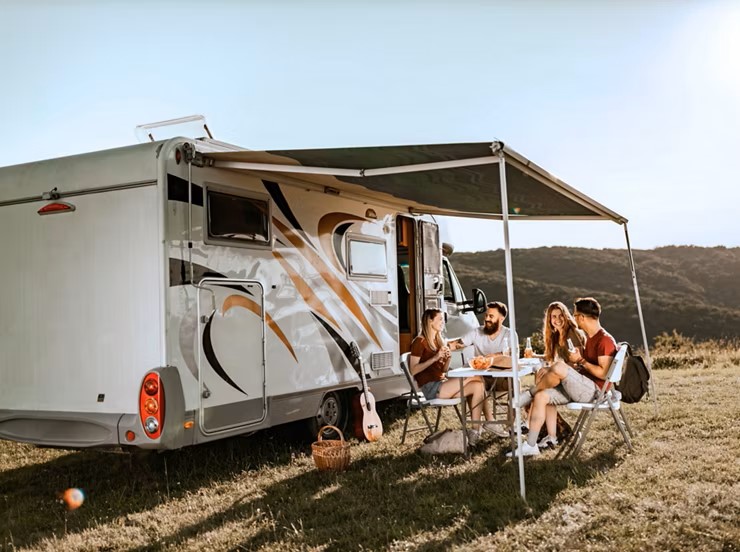 EIne Gruppe junger Menschen sitzt unter dem Vordach eines Wohnmobiles.