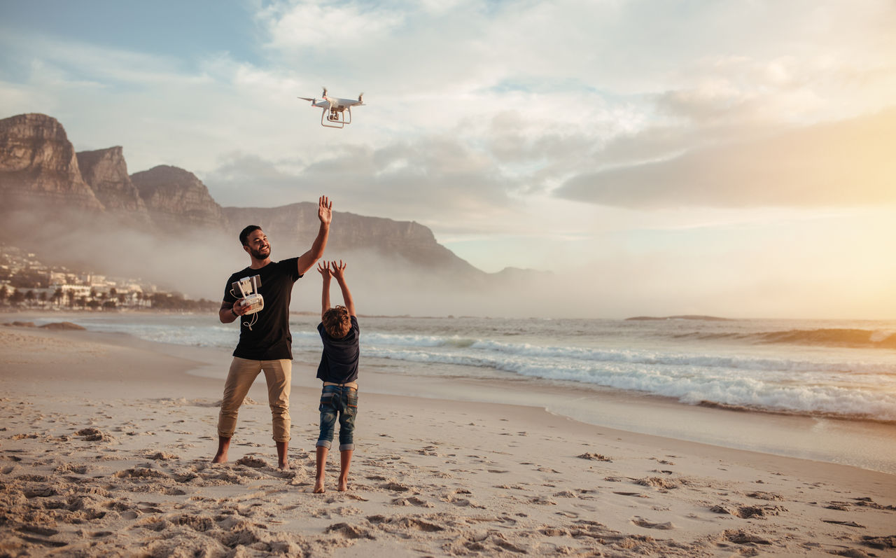 Ein Vater und sein Sohn fliegen eine Drohne mit Fernbedienung am Strand.