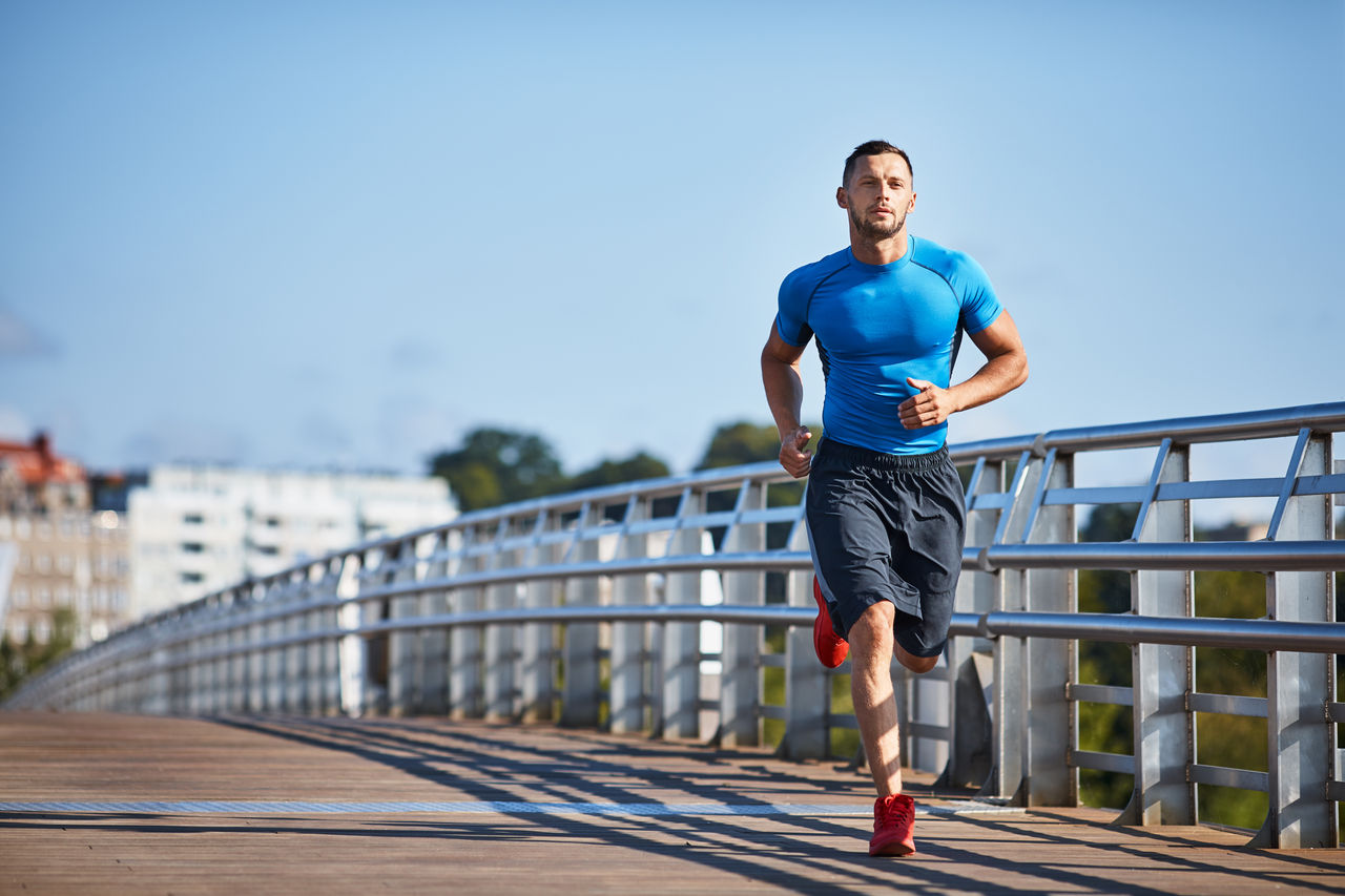 Sportlicher Mann joggt in der Stadt über eine Brücke.