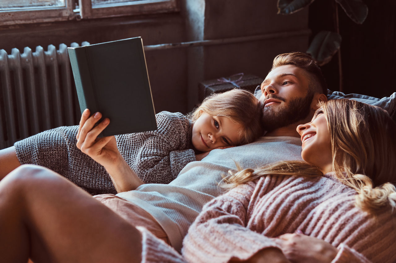 Mutter, Vater und Tochter liegen zusammen mit einem Buch auf einem Bett.