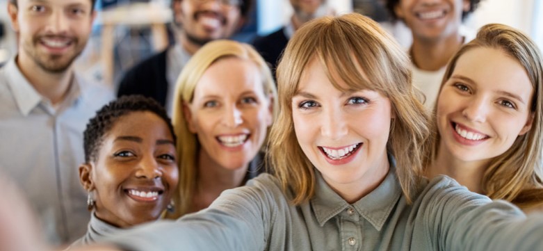Eine Gruppe an Kolleginnen und Kollegen machen ein Selfie und lächeln in die Kamera.