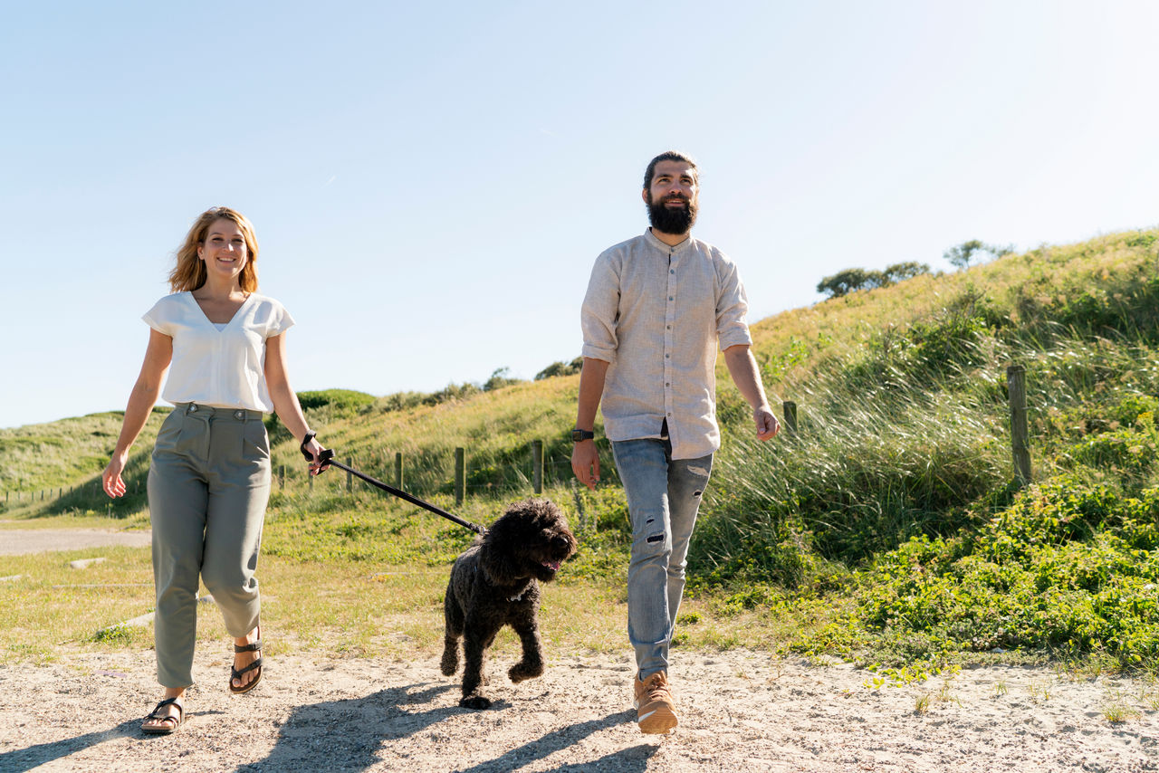 Junges Paar geht mit seinem Hund am Strand spazieren.