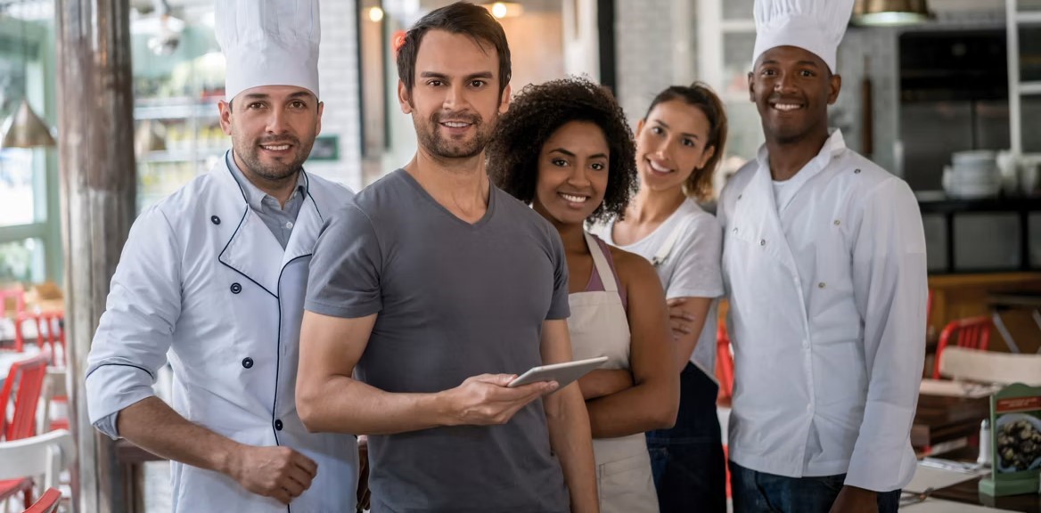 Köche und Mitarbeitende eines Restaurants stehen zusammen und lächeln in die Kamera.