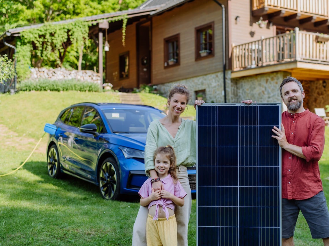 Glückliche Familie posiert mit Photovoltaikmodul beim Aufladen ihres Elektroautos.