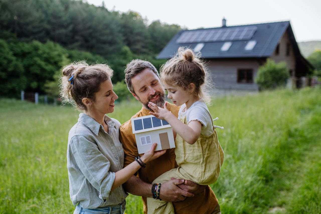 Eine glückliche Familie steht vor Ihrem Haus mit Solarpanelen auf dem Dach.